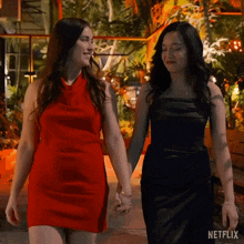 two women in red dresses and black dresses are walking down the street holding hands .