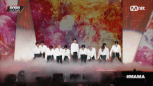 a group of people standing on a stage with a mnet logo in the background