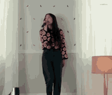 a woman is singing into a microphone in a room with a lamp .