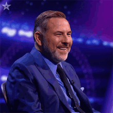 a man in a suit and tie smiles in front of a purple background