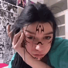a girl with a tattoo on her face is sitting in front of a wall .