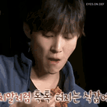 a young man is eating a piece of food with korean writing on the bottom of the image .