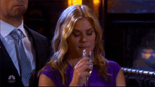a woman in a purple dress is drinking from a glass