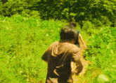 a man in a brown hoodie is walking through a grassy field