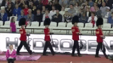 a group of men in red uniforms are marching in front of a hydroden sign .