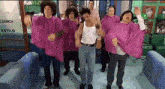 a group of men in pink capes are dancing in a room in a barber shop .