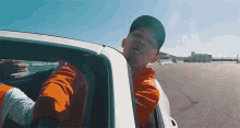 a man wearing a hat and an orange jacket is sitting in a car .