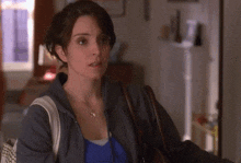 a woman wearing a blue shirt and a grey jacket holds a brown bag