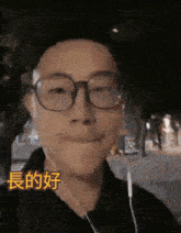 a man wearing glasses and ear buds is smiling with chinese writing behind him