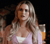a woman in a pink sweater is standing in a dark room and making a surprised face .