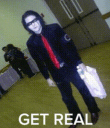 a man in a black suit and red tie is holding a white bag that says get real on the bottom