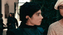 a woman with curly hair is standing next to a man wearing a hat and looking at the camera .