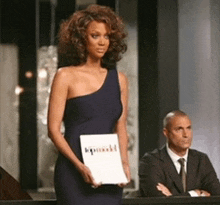 a woman in a blue one shoulder dress is holding a sign that says ' kpnnk ' on it