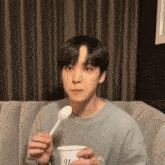 a young man is holding a cup and a spoon in his hands .