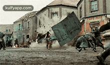 a group of people are running down a street in front of a building that has been destroyed .