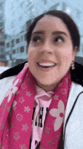 a woman wearing a pink louis vuitton scarf and a white jacket smiles