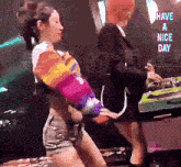 a woman in a rainbow sweater is dancing in front of a sign that says have a nice day