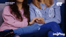 two women are sitting next to each other and holding hands