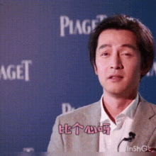 a man in a suit is talking into a microphone in front of a piaget logo .