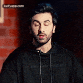 a man with a beard is wearing a black hoodie and looking at the camera .