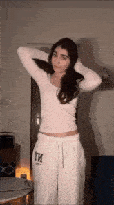 a woman in a crop top and white sweatpants is standing in a living room .