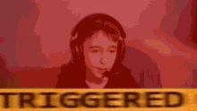 a boy wearing headphones and a microphone is sitting in front of a sign that says triggered