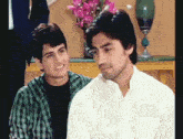 two men are sitting next to each other and one of them is wearing a white shirt
