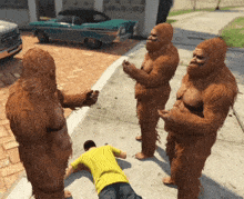 a man in a yellow shirt is laying on the ground surrounded by four bigfoots