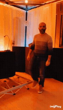 a man with a beard is standing in a room with a table and a microphone .