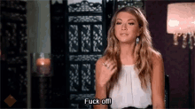 a woman in a white top is sitting in a chair and saying `` fuck off '' .