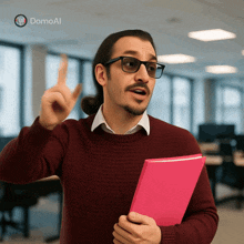 a man wearing glasses and a red sweater is holding a pink book and pointing up