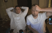 two men are sitting in a room with their hands on their heads