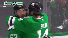 a hockey player wearing a green jersey with the number 14 on it is hugging another player