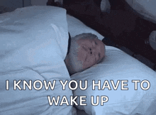 a man is sleeping in a bed with the words `` i know you have to wake up '' written on the bottom .