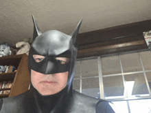 a man in a batman costume is standing in front of a bookshelf