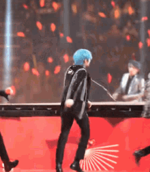 a man with blue hair is dancing on a stage in front of a microphone .