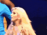 a woman with blonde hair is standing on a stage with a man in a blue shirt behind her