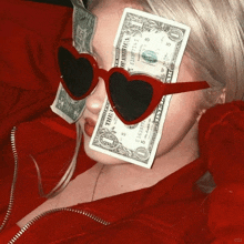 a woman wearing heart shaped sunglasses holds a dollar bill in front of her face