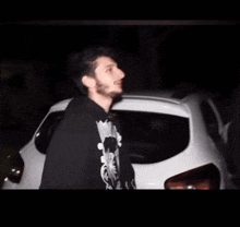 a man with a beard is standing in front of a white car .