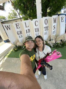 a man and woman standing in front of a sign that says welcome