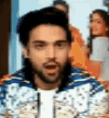 a man with a beard is wearing a blue and white jacket and making a surprised face .