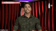 a man in a green shirt is standing in front of a red curtain and making a funny face .