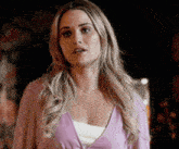 a woman in a pink cardigan and white tank top is standing in a dark room .