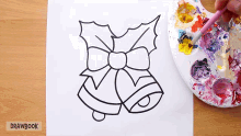 a drawing of a christmas bell with holly and a bow is being painted