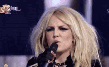a blonde woman singing into a microphone with a star in the lower right corner