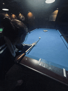 a woman is playing pool in a dark room with a shirt on the wall that says ' kobe '