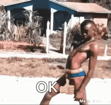 a man in a bikini is giving a thumbs up while standing in front of a house .