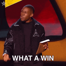 a man in a varsity jacket is holding a piece of paper and says what a win