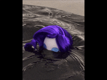 a doll with purple hair is laying on a black cloth