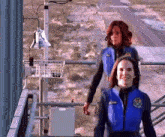 a woman in a blue vest that says ' a. swenson ' on it stands next to another woman